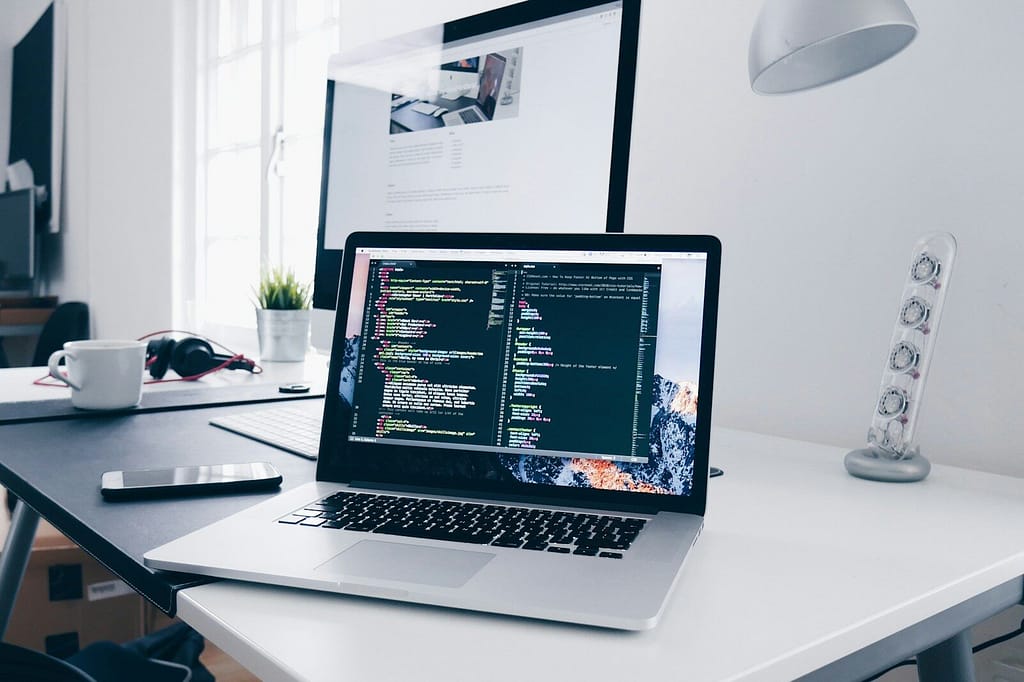 A MacBook with lines of code on its screen on a busy desk. gerilya
